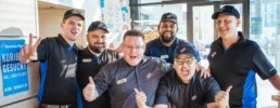 Mitarbeiter von Dominos Pizza Schweiz posieren lächelnd und jubelnd für ein Foto in einer Filiale